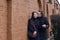 A young man kisses a girl on the cheek. Against the background of a brown brick wall. Dressed in a coat and jacket