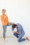 Young man is kneeling and reverently tying shoelaces to his domineering unidentified woman posing on a white background