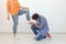 Young man is kneeling and reverently tying shoelaces to his domineering unidentified woman posing on a white background