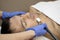 Young man laying on a facial therapy couch covered with the white towel with closed eyes. Facial therapist hands holding