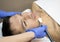 Young man laying on a facial therapy couch covered with the white towel with opened eyes. Facial therapist hands holding