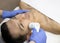 Young man laying on a facial therapy couch covered with the white towel with opened eyes. Facial therapist hands holding