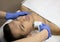 Young man laying on a facial therapy couch covered with the white towel with opened eyes. Facial therapist hands holding