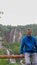 A young man leans on a wooden railing. In the background waterfalls in Plitvice Lakes National Park. Teenager in a blue hoodie