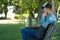 Young man listening to music with wireless earbuds and his laptop on a park bench