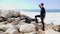 Young man looking at the ocean with hands to head and pointing the finger to the horizon while standing on the rocks. Water splash