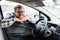 Young man looking through window inside new car, checking it before purchase at modern dealership store. Cheerful guy buying or