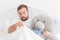 Young man lying in bed with a teddy bear and looking under the blanket