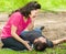 Young man lying down with medical emergency, woman sitting by his side calling for help, outdoors environment