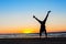 Young man making handstand on the beach. Multicolored sunset background