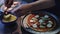 Young man making homemade vegetarian pizza at home adding pineapple topping