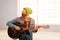 Young man with a mask on face playing the guitar in the light room