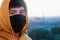 A young man in a medical mask black looks ahead against the blurry background of th