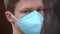 Young man in medical mask looks into the camera; protection against coronavirus COVID-19