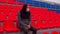 Young man in medical mask sitting on stadium bleachers alone. Sad adult male protecting yourself from diseases at sports