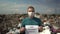 A young man in a medical mask stands with a "keep the planet healthy" poster in front of a garbage dump. Birds fly to