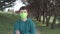 A young man in a medical protective mask on the path against the background of trees in the park.