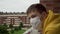 Young man in a medical protective mask sadly looks from the balcony during coronavirus quarantine