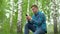 Young man in nature with a phone in his hands. A man sits on a stump in a birch forest and leads works through a