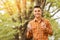 Young man in orange checkered shirt with smart phone and coffee in park in autumn