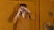 Young man in orange glasses with old photo camera stands against background of brown doors in room. Stylish male