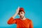 Young man in orange hat and t-shirt touches his head as if he remembered something on blue background