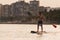 Young man paddle surfs in the mediterranean sea leaving the city and the buildings behind