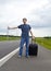 The young man pending on road with a suitcase