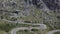 A young man pilots a drone which is going away from a curved rural road.