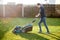 Young man in a plaid shirt and jeans mows lawn