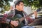 Young man play solo guitar while sitting on park bench