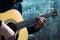 Young man playing an acoustic guitar on the background of a concrete wall