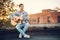 Young man playing guitar in city on sun rays background. Handsome hippie style guitarist engrossed on music outdoors. Concept of