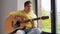 Young man playing guitar sitting on windowsill