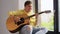 Young man playing guitar sitting on windowsill