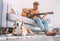 Young man plays on guitar sitting on the sofa at home and beagle