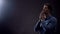 Young man praying in dark room under blessed light from heaven, Christianity