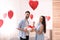 Young man presenting gift to his girlfriend in room decorated with heart shaped balloons. Valentine`s day celebration