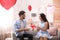 Young man presenting gift to his girlfriend in room decorated with heart shaped balloons. Valentine`s day celebration