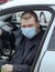 A young man in a protective mask drives a car. Portrait of a Caucasian man in a medical mask. A man is going to rest outside