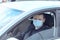 A young man in a protective mask drives a car. Portrait of a Caucasian man in a medical mask. A man is going to rest outside
