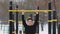 Young man pulls himself up on a horizontal bar on the street in winter.