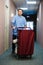 Young man pushing a housekeeping cart laden with clean towels, laundry and cleaning equipment in a hotel as he services