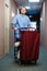 Young man pushing a housekeeping cart laden with clean towels, laundry and cleaning equipment in a hotel as he services