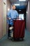 Young man pushing a housekeeping cart laden with clean towels, laundry and cleaning equipment in a hotel as he services