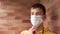 Young man is putting on a protective medical mask against a brick wall