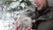 Young man with a rabbit. The guy gently hugs a gray fluffy bunny in winter snowy forest. Travel with pet.