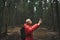 Young man in a red jacket stands in the woods during a hike and takes a photo on a smartphone camera.Portrait of hiker man in