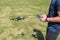 Young man with remote control cell phone flying drone. Sunny green nature