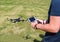 Young man with remote control cell phone flying drone. Sunny green nature